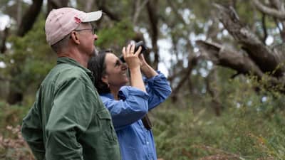 Peter Turnbull and Susan Ball looking through binoculars at their bushland property.